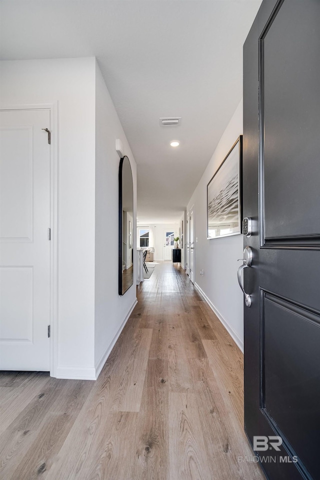hallway featuring baseboards, light wood finished floors, and visible vents