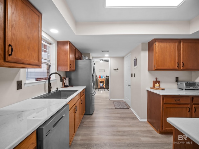 kitchen with sink, stainless steel dishwasher, light stone counters, and light wood-type flooring