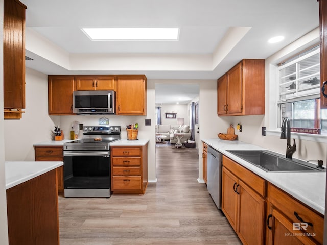 kitchen featuring sink, light hardwood / wood-style flooring, a skylight, stainless steel appliances, and a tray ceiling