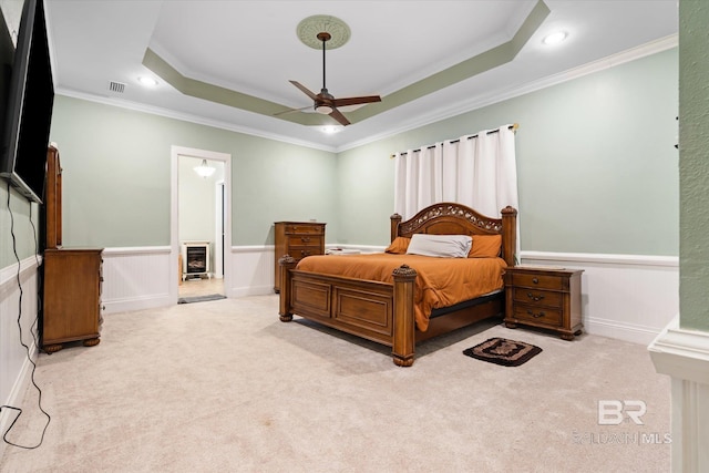 carpeted bedroom with a raised ceiling, ornamental molding, connected bathroom, and ceiling fan