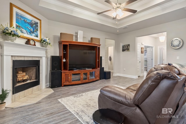 living room with a fireplace, light hardwood / wood-style flooring, a raised ceiling, and ceiling fan