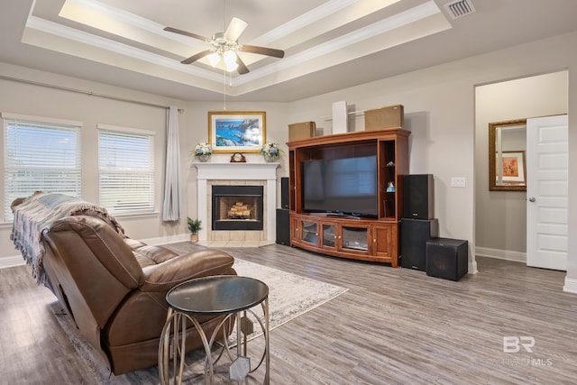 living room featuring a tile fireplace, a raised ceiling, crown molding, hardwood / wood-style flooring, and ceiling fan