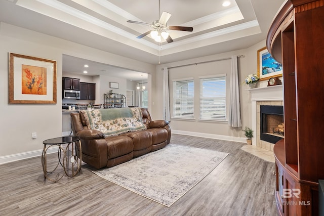 living room featuring hardwood / wood-style floors, ceiling fan, ornamental molding, a tray ceiling, and a tiled fireplace