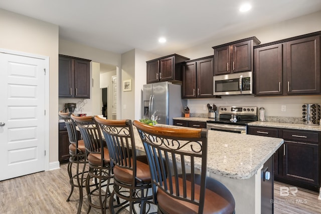 kitchen with a breakfast bar, dark brown cabinetry, stainless steel appliances, light hardwood / wood-style flooring, and a kitchen island