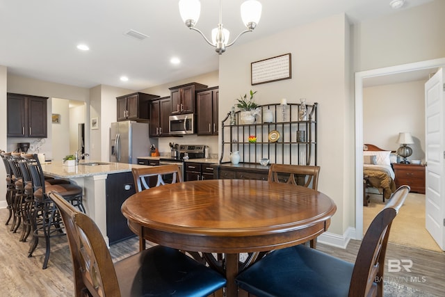 dining area with sink, light hardwood / wood-style floors, and an inviting chandelier