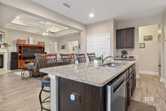 kitchen featuring a kitchen island with sink, a raised ceiling, sink, stainless steel dishwasher, and a breakfast bar area