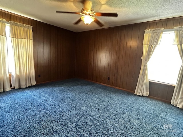 spare room with a ceiling fan, carpet, wooden walls, and a textured ceiling