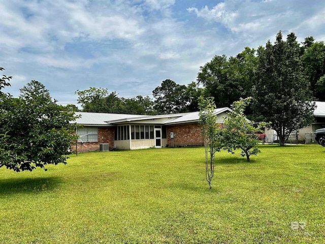back of property with a yard, central AC, metal roof, and a sunroom