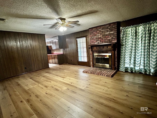 unfurnished living room with wood walls, hardwood / wood-style floors, a ceiling fan, a textured ceiling, and a fireplace