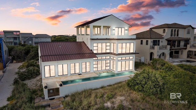 7276 Kiva Way, Gulf Shores, AL 36542 - back of property at dusk featuring a balcony, stucco siding, a standing seam roof, and metal roof