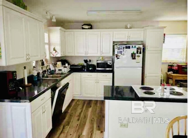kitchen featuring freestanding refrigerator, stainless steel microwave, wood finished floors, white cabinetry, and dark countertops