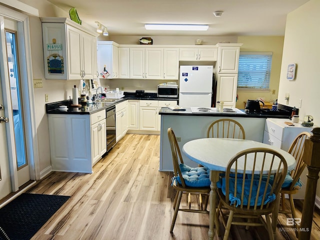 kitchen with freestanding refrigerator, stainless steel microwave, dishwasher, light wood-style flooring, and dark countertops
