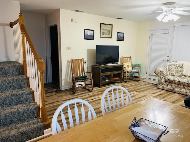 living area featuring light wood-type flooring, ceiling fan, baseboards, and stairway