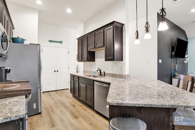 kitchen featuring stainless steel appliances, sink, decorative light fixtures, a kitchen breakfast bar, and light hardwood / wood-style floors