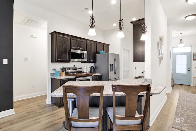 kitchen with appliances with stainless steel finishes, hanging light fixtures, light wood-type flooring, and kitchen peninsula