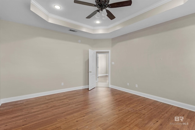 spare room featuring crown molding, a tray ceiling, wood-type flooring, and ceiling fan