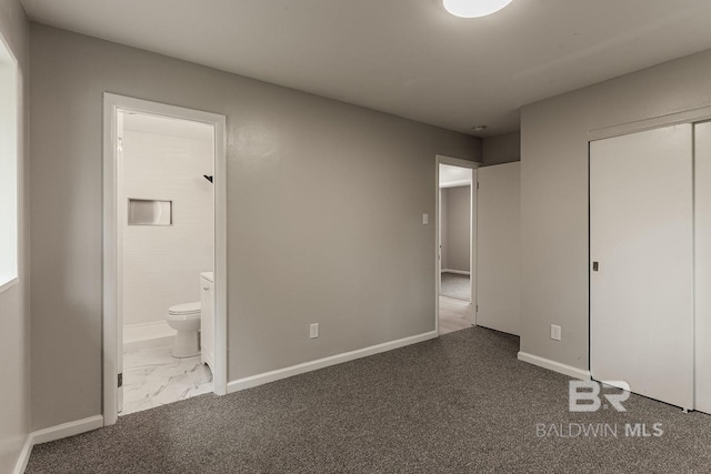 unfurnished bedroom featuring ensuite bathroom, a closet, and dark colored carpet