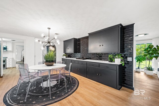 kitchen featuring stove, light hardwood / wood-style flooring, an inviting chandelier, pendant lighting, and backsplash