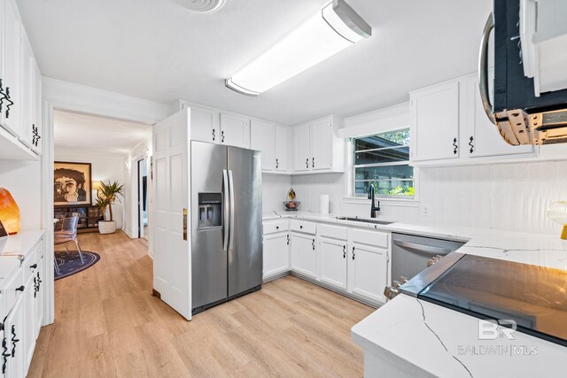 kitchen featuring appliances with stainless steel finishes, white cabinets, sink, light stone counters, and light wood-type flooring