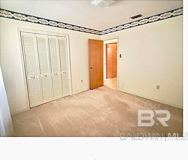 unfurnished bedroom with light colored carpet, a textured ceiling, and a closet