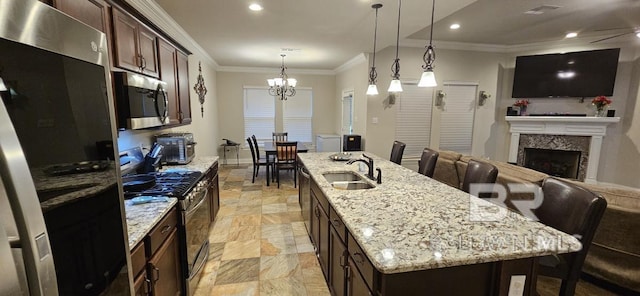 kitchen featuring appliances with stainless steel finishes, light stone counters, a kitchen island with sink, light tile patterned floors, and a premium fireplace