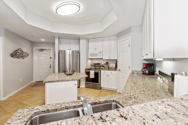 kitchen with a tray ceiling, a center island, appliances with stainless steel finishes, white cabinets, and a sink