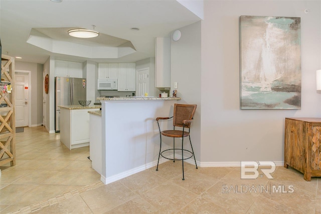 kitchen featuring white microwave, a peninsula, white cabinetry, baseboards, and a raised ceiling