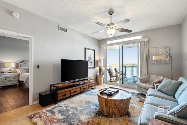 living area featuring tile patterned flooring, ceiling fan, visible vents, and a textured ceiling