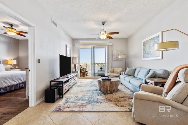 living area featuring a textured ceiling, tile patterned flooring, visible vents, a ceiling fan, and baseboards