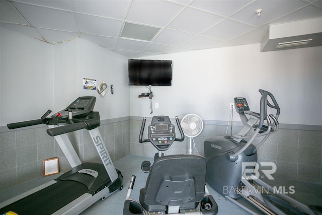 workout room with a wainscoted wall, tile walls, and a drop ceiling