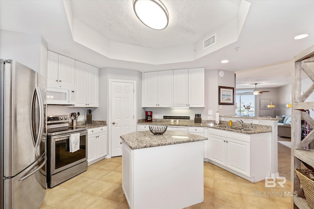 kitchen with a peninsula, a sink, visible vents, appliances with stainless steel finishes, and a raised ceiling