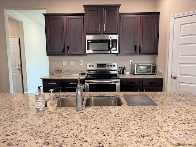 kitchen with dark brown cabinets, sink, light stone countertops, and stainless steel appliances