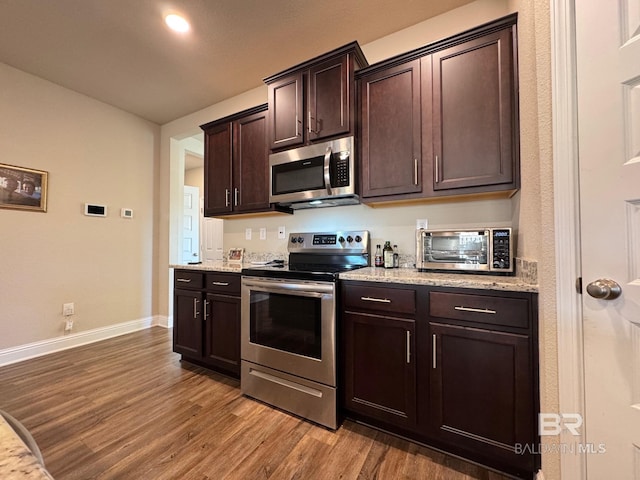 kitchen featuring dark brown cabinetry, light stone countertops, stainless steel appliances, and hardwood / wood-style flooring