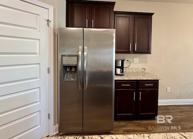 kitchen with stainless steel fridge, dark brown cabinets, light stone countertops, and dark hardwood / wood-style floors