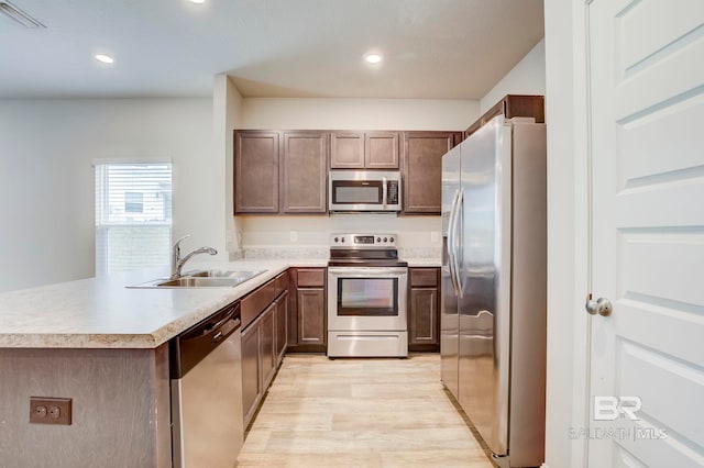 kitchen with kitchen peninsula, sink, stainless steel appliances, and light hardwood / wood-style floors