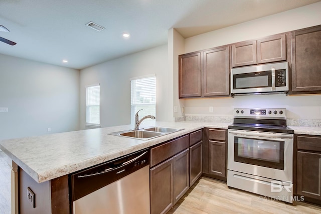 kitchen with kitchen peninsula, light wood-type flooring, dark brown cabinetry, stainless steel appliances, and sink