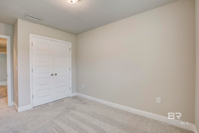 unfurnished bedroom featuring a textured ceiling, light colored carpet, and a closet