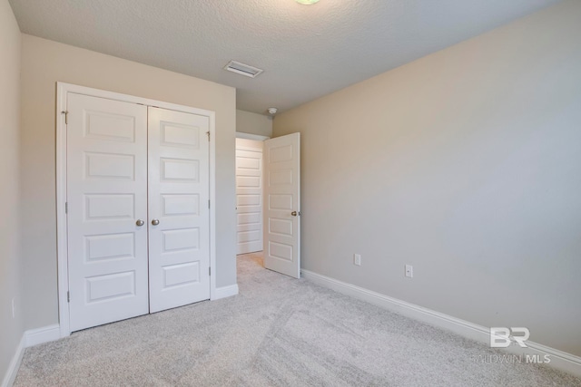 unfurnished bedroom featuring a closet, light colored carpet, and a textured ceiling