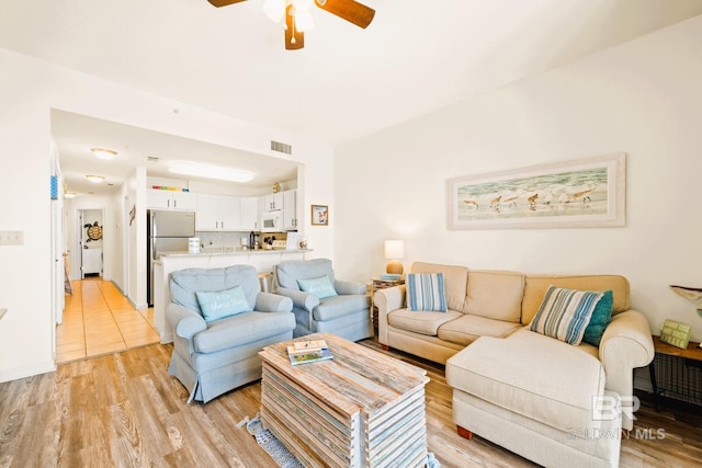 living room with visible vents, light wood-style flooring, and a ceiling fan