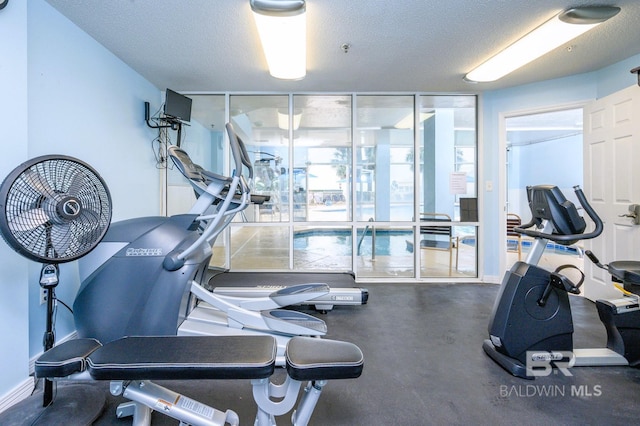 exercise room with expansive windows, a textured ceiling, and baseboards