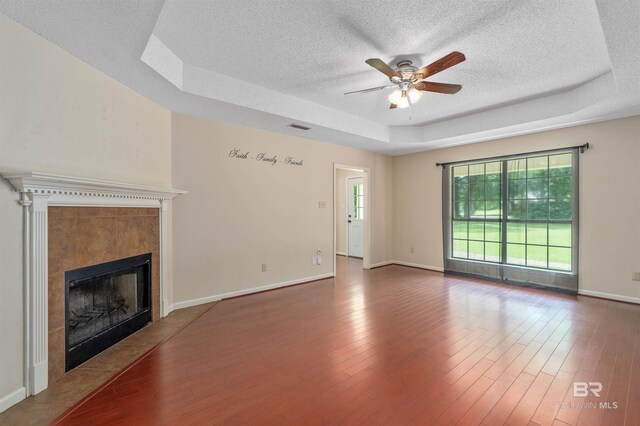 25779 Austin Rd, Daphne, AL 36526 - unfurnished living room featuring a raised ceiling, a textured ceiling, a ceiling fan, a tiled fireplace, and baseboards