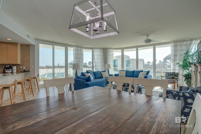 dining room with ceiling fan with notable chandelier and a wall of windows