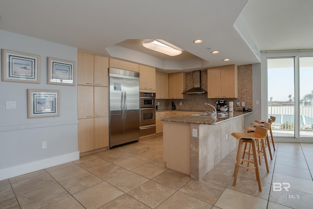 kitchen with decorative backsplash, a kitchen breakfast bar, wall chimney exhaust hood, kitchen peninsula, and stainless steel appliances