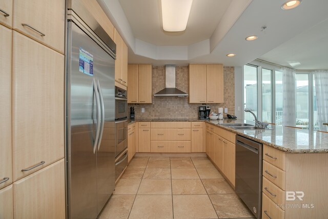 kitchen featuring wall chimney range hood, sink, appliances with stainless steel finishes, and light brown cabinets