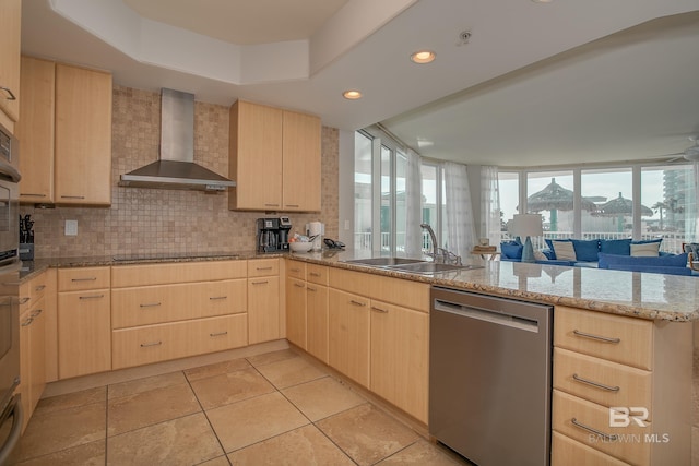 kitchen featuring stainless steel dishwasher, light brown cabinets, kitchen peninsula, and wall chimney range hood