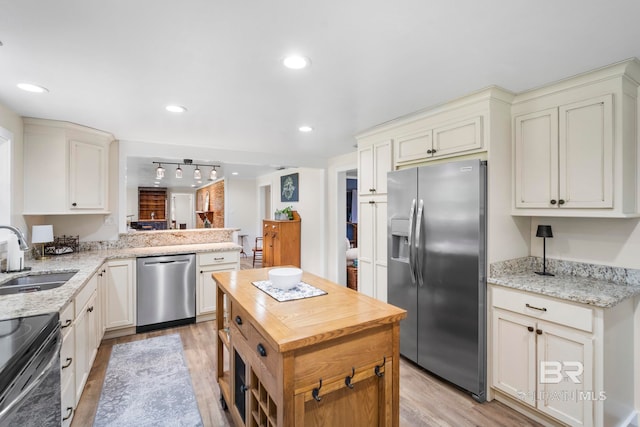 kitchen with light stone countertops, appliances with stainless steel finishes, light wood-type flooring, sink, and kitchen peninsula