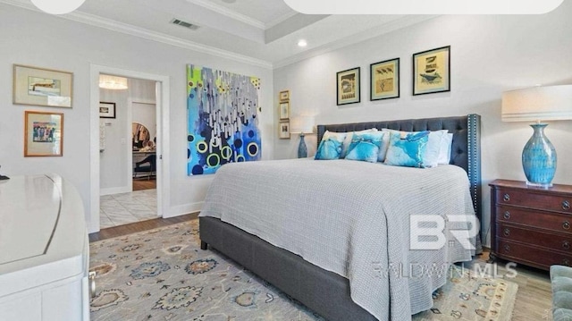 bedroom with a tray ceiling, visible vents, crown molding, and wood finished floors