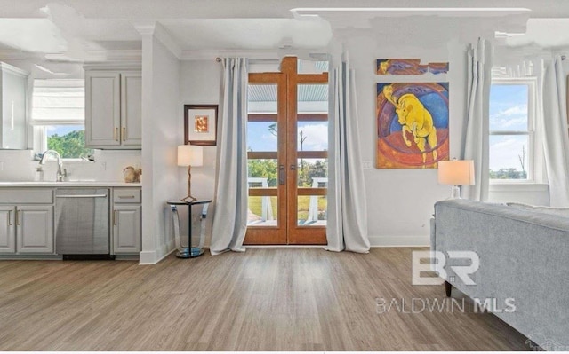 interior space with a sink, baseboards, ornamental molding, french doors, and light wood finished floors