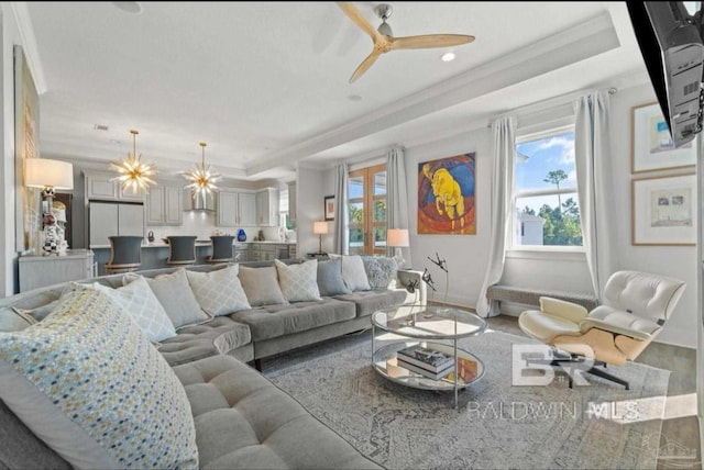 living area with ornamental molding, a raised ceiling, a wealth of natural light, and wood finished floors