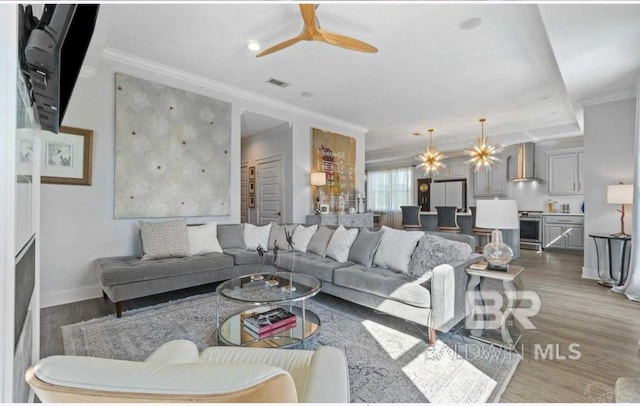 living room with crown molding, visible vents, wood finished floors, baseboards, and ceiling fan with notable chandelier